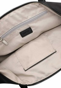 Binnenkant van een zwarte stoffen tas met een beige voering, voorzien van een ritsvak en een plat steekvak. Stiksels zijn zichtbaar langs de randen.