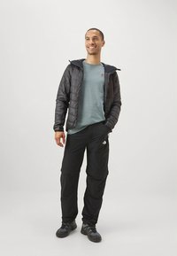 Sort puffjakke med hette, grå langermet skjorte og svarte bukser med logo. Brukt med solide svarte sko. Enkelt design.