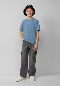 Lichtblauw katoenen t-shirt met een klein zwart logo, gecombineerd met losse grijze cargo shorts met zijzakken en witte sneakers.