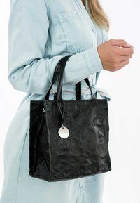 Svart läder tote-väska med en texturerad yta och dubbla handtag, med en metallisk logotyp och minimalistisk design.