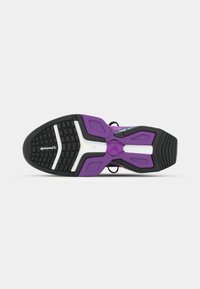 Suola di scarpa sportiva con una base in gomma nera, dettagli viola, motivi di grip testurizzati e rifiniture bianche per stabilità e trazione.