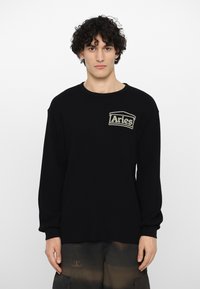 Sort ribbet langærmet sweatshirt med rund hals, der har et syet "Aries" logo-patch på venstre brystområde. Casual fit.