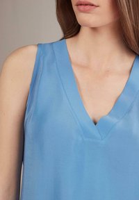 Ljust blå ärmlös topp med V-ringning, slät textur och avslappnad passform, som erbjuder en minimalistisk och modern estetik.
