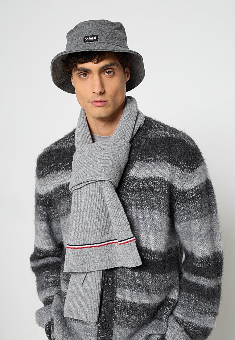 Cappello bucket grigio con logo, cardigan grigio a righe e sciarpa grigia a coste con accenti rossi e blu, tutti in una texture morbida.