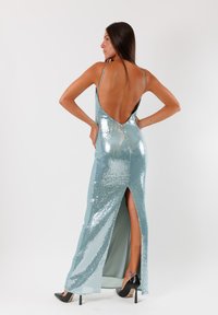 Abito da sera in paillettes di colore azzurro chiaro, con schiena in caduta, alta apertura laterale e spalline sottili. Tessuto liscio impreziosito da paillettes luccicanti.