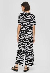 Combinaison à imprimé zèbre noir et blanc avec des manches courtes, des jambes larges et une finition texturée. Portée avec des sandales à plateforme noires.