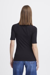 Schwarzes, tailliertes T-Shirt mit kurzen Ärmeln, glatter Textur und Rundhalsausschnitt. Kombiniert mit weiten blauen Jeans mit Gesäßtaschen.