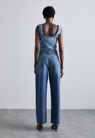 Denim jumpsuit with a zip closure, wide leg design, and sleeveless cut. Features back pockets and a mid-blue wash with subtle texture.
