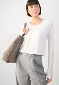 White cropped cardigan over a light top, paired with light gray pinstriped trousers. Holding a gray suede shoulder bag with a strap.
