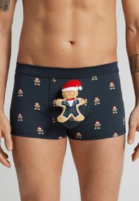 Svarta boxershorts med ett heltryck av pepparkaksgubbar i julkläder, med en mjuk pepparkaksgubbe som accessoar fram.