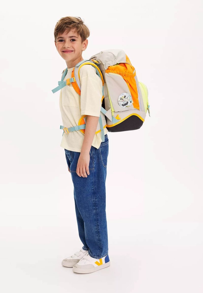 Der Rucksack besteht aus einer Mischung aus grauen, orangen und gelben Materialien, mit verstellbaren Trägern, Seitentaschen und einem Charakter-Patch auf der Rückseite.