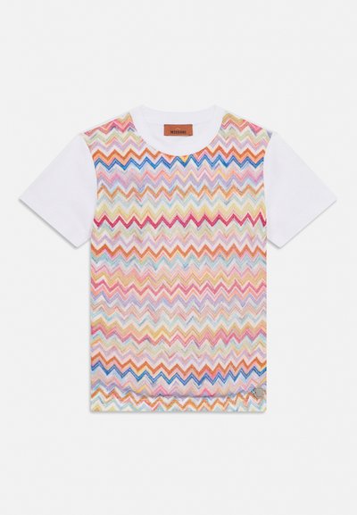 Λευκό κοντομάνικο T-shirt με πολύχρωμο σχέδιο ζιγκ-ζαγκ πλέξης στο μπροστινό μέρος και μικρό στρογγυλό ασημί λογότυπο κοντά στο κάτω τελείωμα.