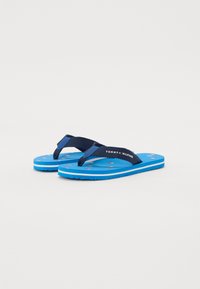 Blå flip-flops med marineblå stropper, teksturert såle med små røde prikker, og "TOMMY HILFIGER"-logo på stroppen. Solid gummisåle.