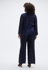 Tumesinist kaheosaline volditud rõivakomplekt, mis koosneb pikkade varrukatega ülikonnast ja laiade säärtega pükstest, valmistatud kerge ja tekstuuriga kangast.