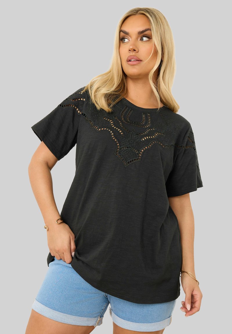 Musta lyhythihainen t-paita, jossa on monimutkainen leikkausyksityiskohta kauluksessa. Yhdistetty vaaleansinisiin farkkushortseihin.