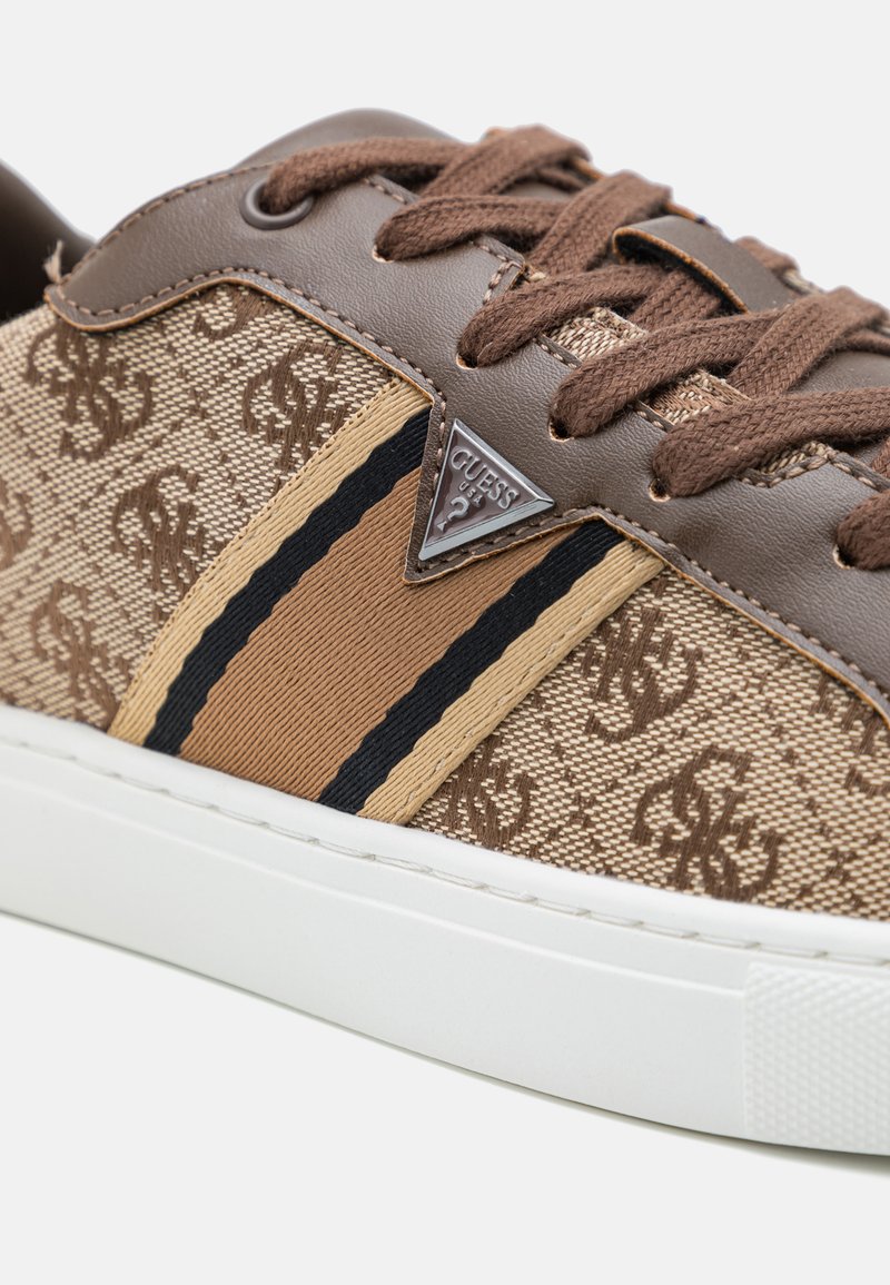 Zapatillas de tela marrón con un patrón texturizado, que presentan detalles en cuero marrón, una franja en beige y negro, y una suela de goma blanca.