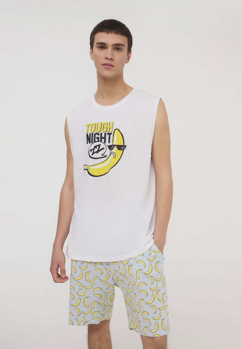 Camicetta bianca senza maniche con il testo "TOUGH NIGHT" e una grafica di banana. Pantaloni corti grigi chiari con un motivo ripetuto di banane gialle.