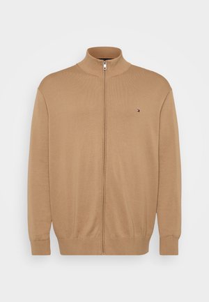 Beige zip-up sweater van ribgebreide stof, met een hoge kraag en een klein logo-accent aan de linkerkant van de borst.