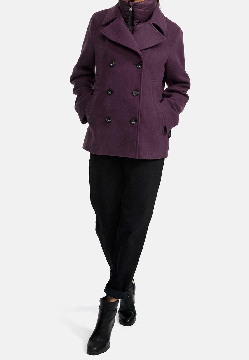 Manteau violet croisé en mélange de laine, doté de grands boutons noirs, d'un large col cranté et de poches sur les côtés, associé à un pantalon noir et des bottines.