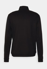 Pull noir à manches longues avec un col montant, vu de dos sur un fond gris clair.