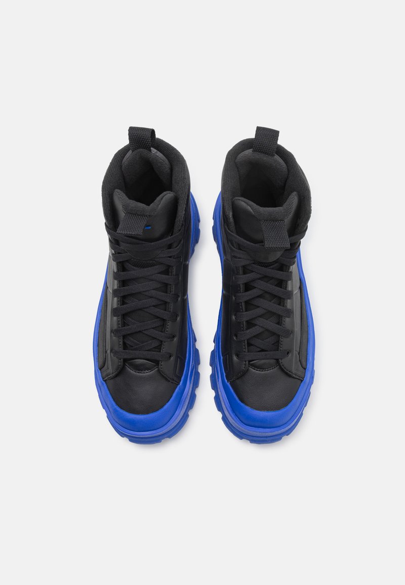 Zapatillas altas con parte superior negra de textura suave y suela gruesa azul. Incluyen cordones negros y lengüetas en el talón.