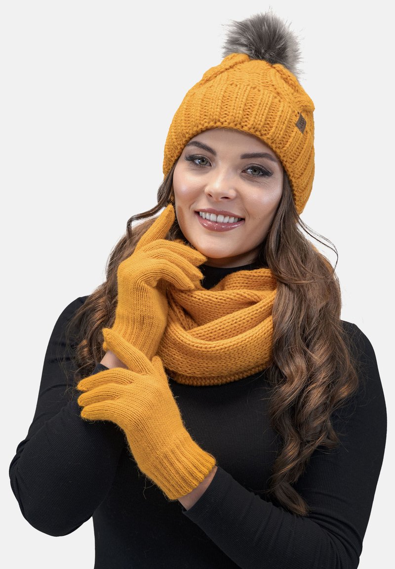 Sennepsgul strikket hat med pompon, matchende tørklæde og handsker, med ribbet struktur og blødt stof.