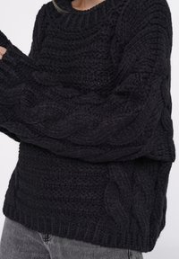 Schwarzer Strickpullover mit Zopfmuster, gerippten Bündchen und Saum, lockerem Schnitt und strukturiertem Stoff. Ideal für Freizeitkleidung.