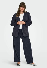 Mornarska teksturirana srajca in usklajene široke hlače, ki ponujajo strukturirano zasnovo, odprt sprednji del in velike zaklopne žepe. Nežen lesk.