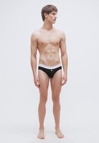 Caleçons pour hommes noirs avec une ceinture blanche. Le tissu est lisse, la coupe est ajustée et porte un petit logo sur la ceinture.