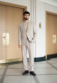 Svetle béžový oblek s upraveným sakem a kalhotami. Spárován se krémovým svetrem a hnědými koženými botami. Hladká textura; minimalistický design.