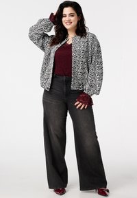 Zwart-wit zebraprint bomberjack over een bordeaux kanten top, gecombineerd met hooggetailleerde zwarte wijde broekspijpen en bordeaux puntige schoenen.