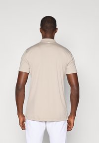 Beige kortermet polo skjorte med en subtil ribbet krage, glatt tekstur og en liten logodetalj på baksiden av nakken. Enkel og ren design.