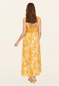 Maxikleid im gelben Blumenmuster mit ärmellosem Design und offenem Rücken. Strukturierter Stoff; mit weißen und pinken Blumenakzenten.