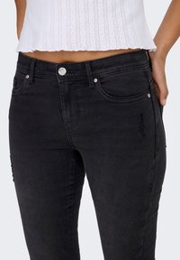 Black denim jeans with a fitted design, featuring a silver button closure, front and back pockets, and subtle embroidered detailing.