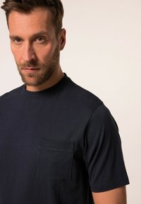 Námořnická modrá bavlněná tričko s kulatým výstřihem, krátkými rukávy a náprsním kapsičkou na levé straně hrudi. Hladká textura, ležérní design.