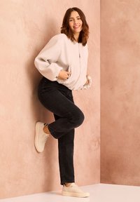 Giacca bomber in pile grigia chiara, con chiusura zip e maniche oversize; abbinata a jeans neri a gamba dritta e sneakers cream con plateau.