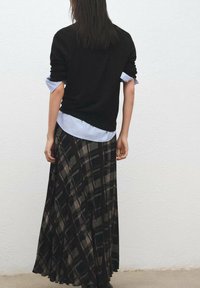 Čierny sveter vrstvený cez svetlomodrú pruhovanú košeľu, nosený s dlhou čiernou a károvanou sukňou v béžových a sivých tónoch.