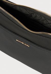 Clutch de nylon negro con cremallera dorada y logo de la marca. Textura suave con un interior espacioso y un patrón sutil en el forro.