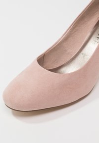 Gros plan sur une ballerine en daim rose pâle avec bout arrondi et texture lisse sur fond blanc.