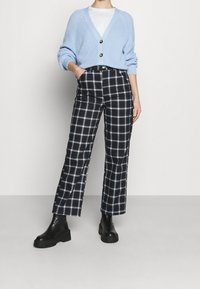 Vaaleansininen ribbed-neulecardigan, jossa on kaksi nappia, yhdistettynä musta-valkopilkullisiin korkeavyötäröisiin housuihin ja mustiin paksupohjaisiin saappaisiin.