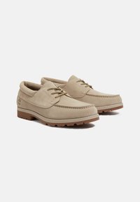 Scarpe in suede beige con design mocassino, lacci frontali e suola in gomma. Presentano una punta cucita e un logo sul tallone.