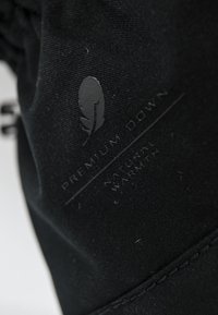 Tessuto nero con un logo che presenta una piuma e la scritta "Calore Naturale Premium Down", che enfatizza le sue capacità termiche.