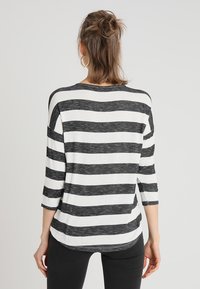 Chemise à rayures noires et blanches avec des manches trois quarts, en tissu doux, ourlet arrondi et coupe décontractée. Vue arrière montrée.