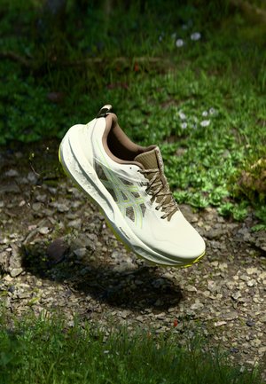 Shoe atlético bege claro com uma parte superior texturizada, detalhes castanhos e um design refletor. Apresenta uma sola almofadada e atacadores.