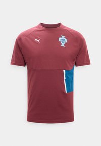 T-shirt de sport bordeaux à manches courtes avec une poche latérale bleue, logo Puma sur la poitrine droite et un emblème de blason bleu et blanc sur la poitrine gauche.