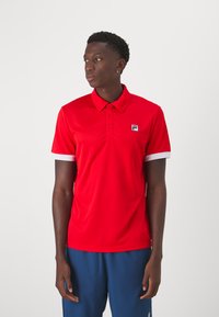 Polo rouge à manches courtes, accents blancs au niveau des poignets et logo Fila sur la poitrine. Fabriqué en matériau lisse et léger.