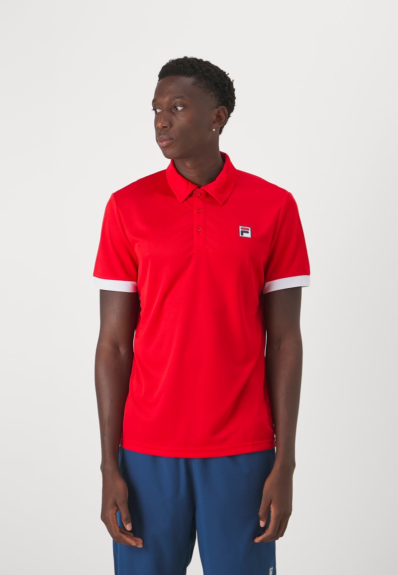 Polo rouge à manches courtes, accents blancs au niveau des poignets et logo Fila sur la poitrine. Fabriqué en matériau lisse et léger.