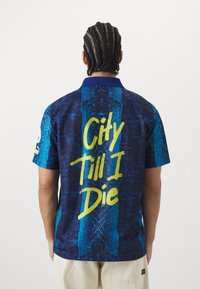 Texturovaná košile s krátkým rukávem v modré a námořnické barvě s širokým modrým límcem, na zadní straně s grafikou "City Till I Die" v jasně žluté barvě.