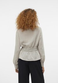 Lys grå bluse med teksturert stoff, samlet liv og lange ermer. Har en glatt finish og knappdetaljer på mansjettene.