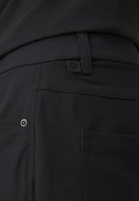 Pantaloni negri din material elastic. Au un nasture sigur, buzunare plate și o patch logo subtilă lângă talie.